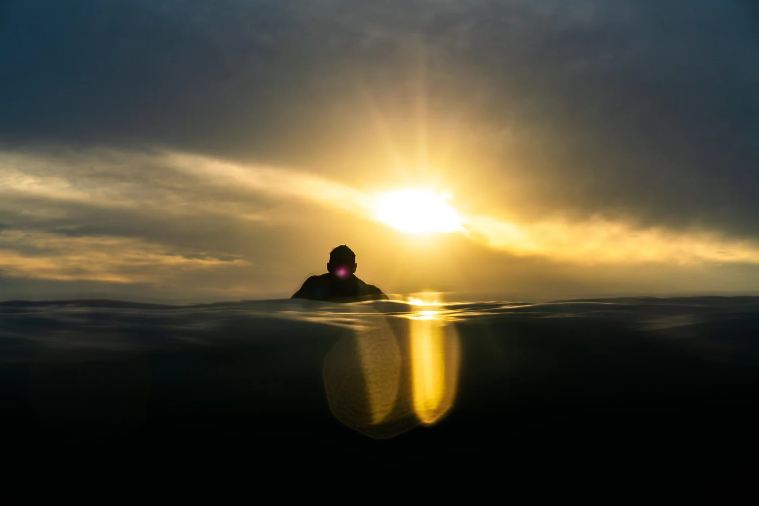 A person in the ocean beneath a golden sunrise