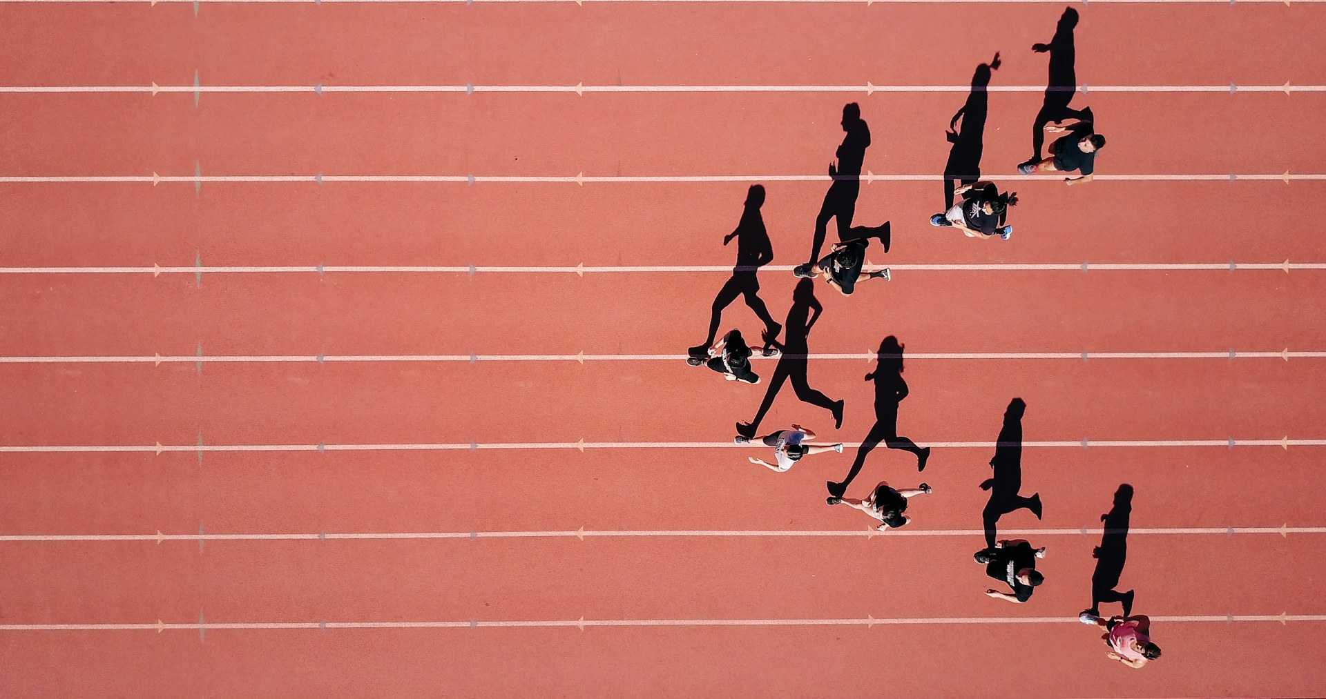 Runners and their shadows crossing the lanes of a red athletics track